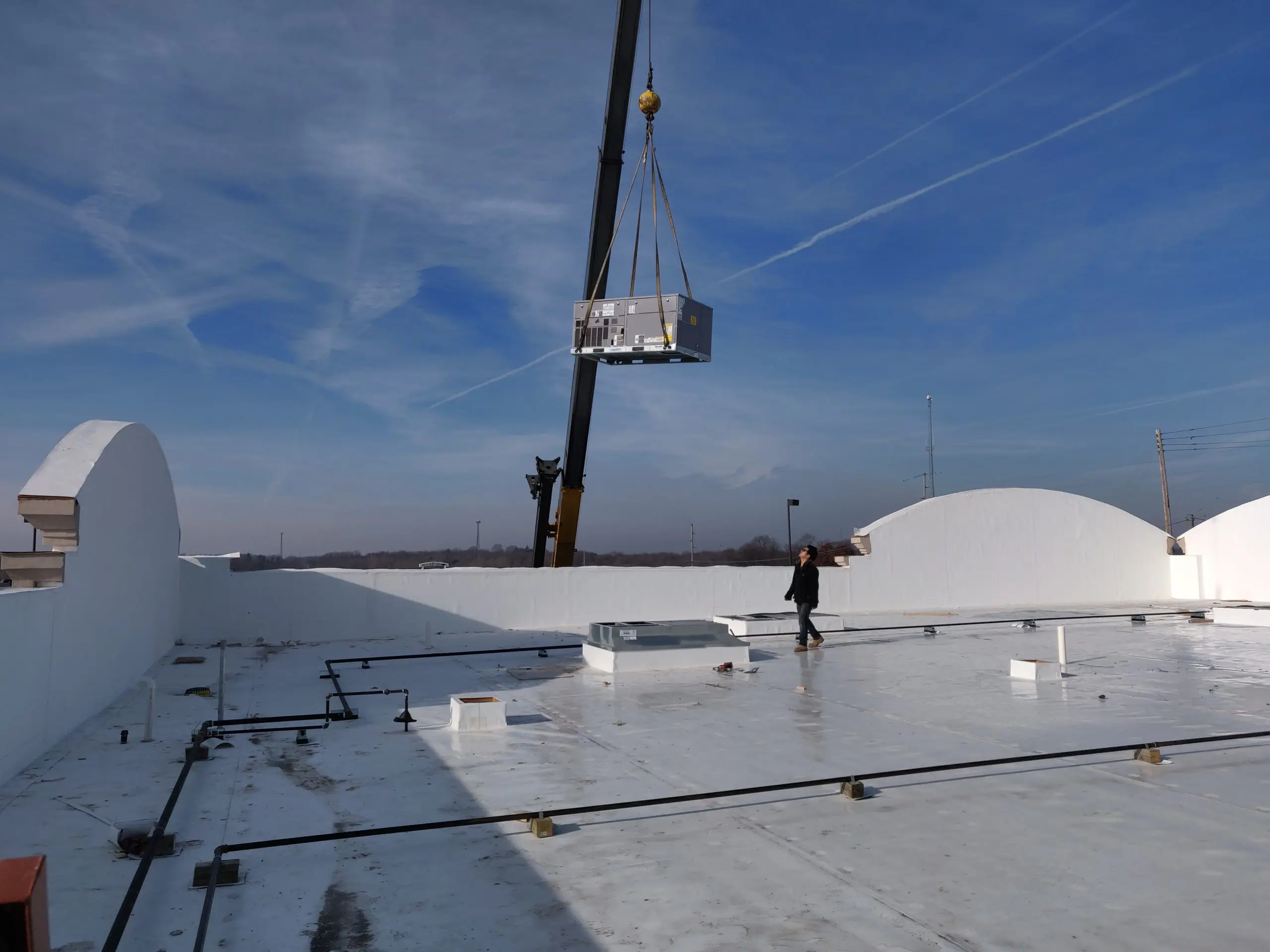 A crane lifting a commercial air conditioning unit onto a roof top.