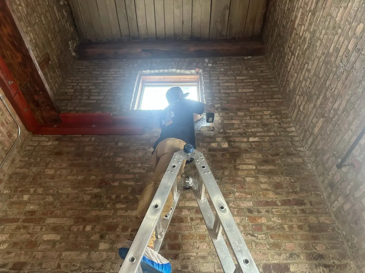 A HVAC technician standing on a ladder holding an electric drill.