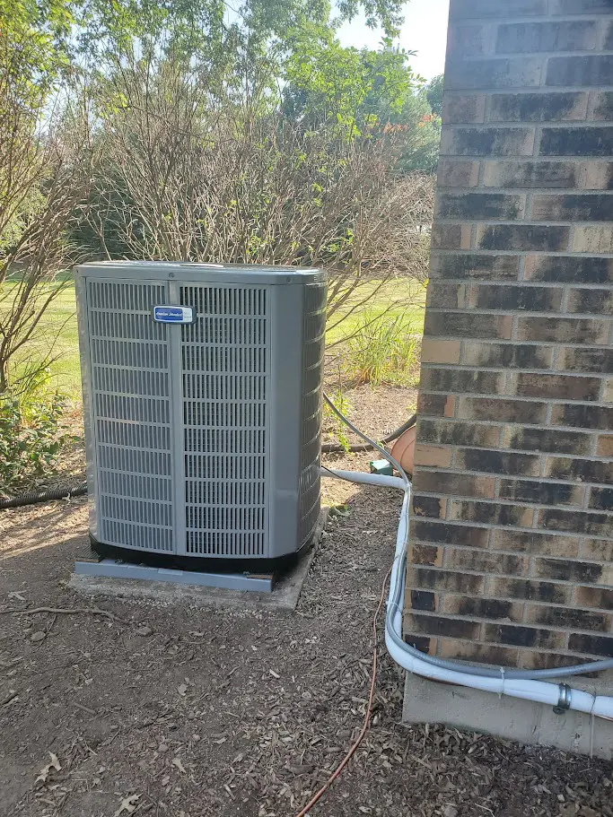 An air conditioner on the ground near a brick house in Naperville IL.