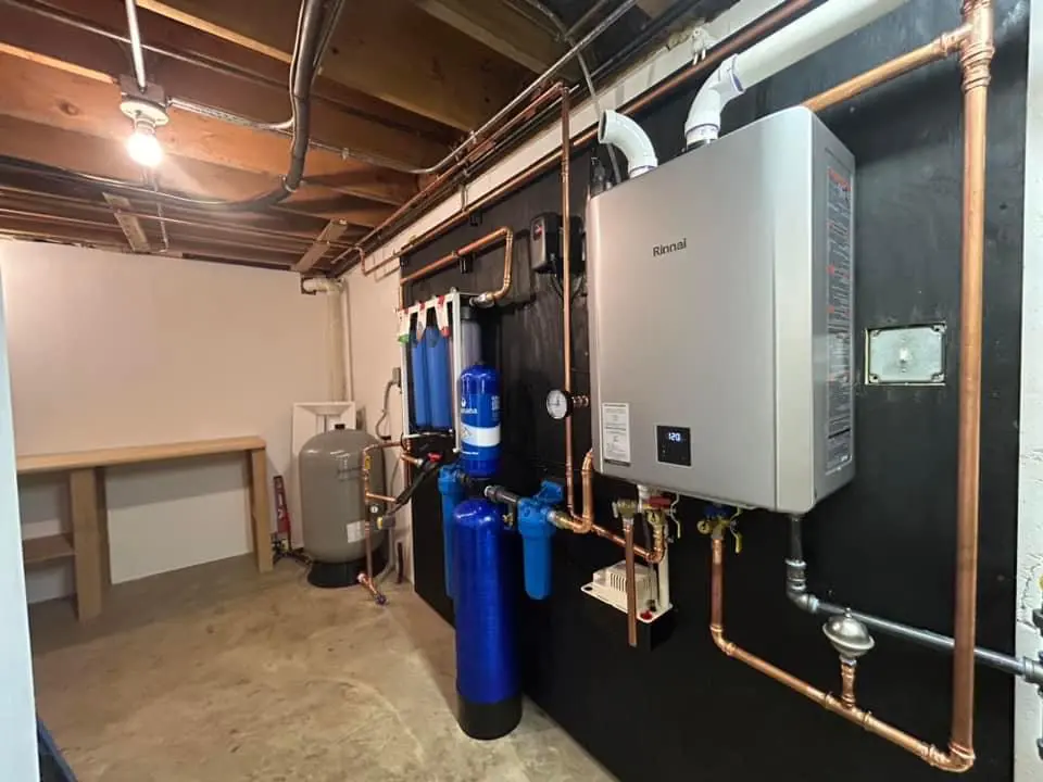 Whole home water filtration system next to a tankless water heater in a basement.
